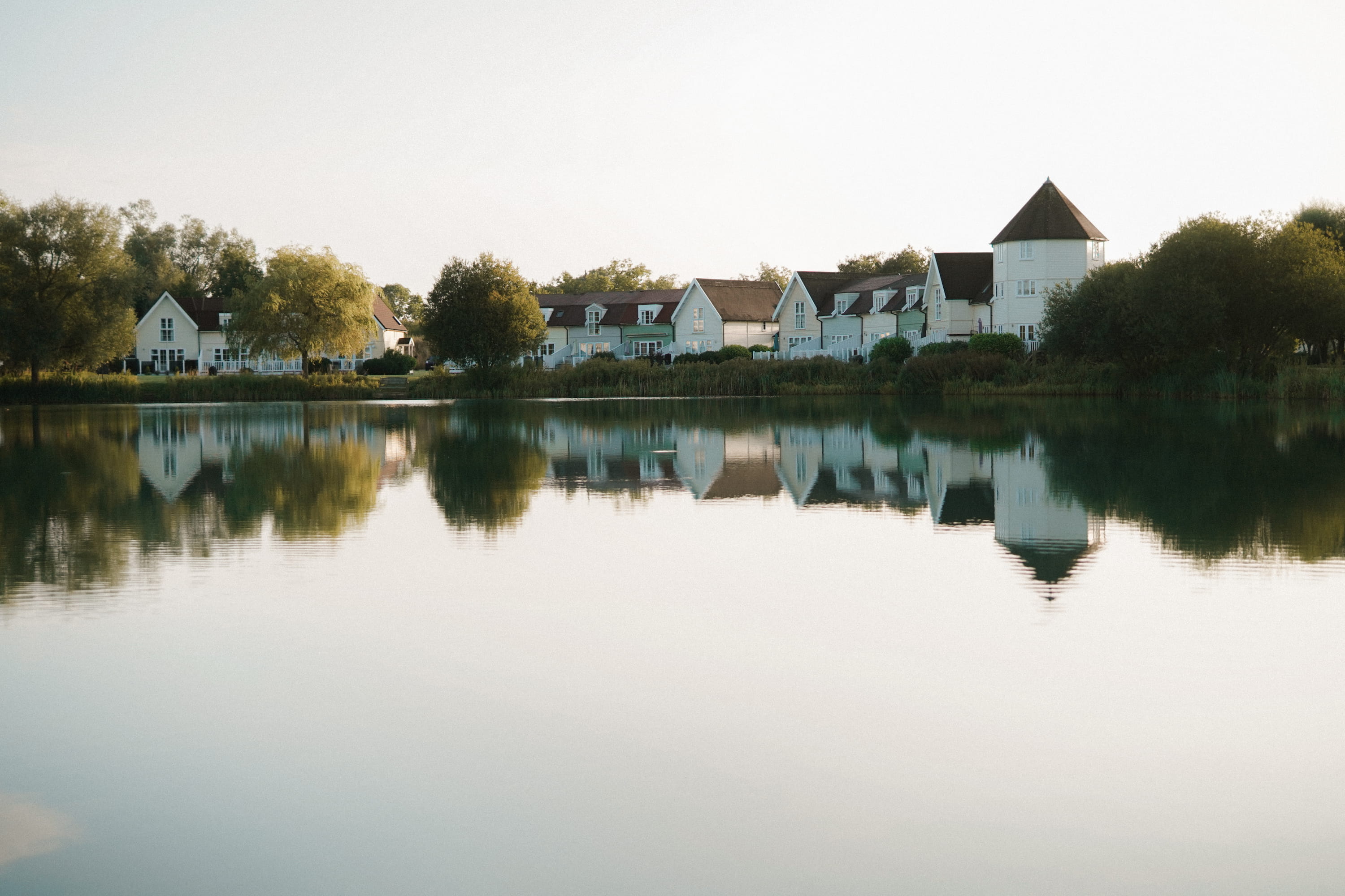 A row of white lakeside houses reflected in still water at golden hour