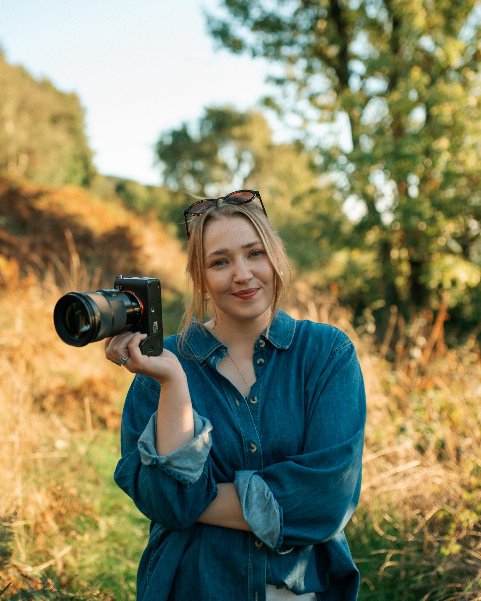 Lily Taylor on a mountain trail, camera round her neck and pines behind her